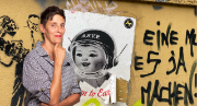 Photo de Sibylle Rau La photo est composée comme un collage artistique. À gauche, on voit Sybille Rau. Elle se tient debout en souriant, la main droite posée sous son menton. Elle a l’air pensive. Le fond est un mur jaune avec une affiche déchirée et plusieurs graffitis. Un des graffitis représente un homme avec une cravate. On peut aussi lire des mots en allemand: «eine», «es» ou «ja». L’affiche représente une fillette portant un casque sur fond blanc.  